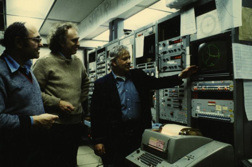 Three men looking at a monitor in a control room