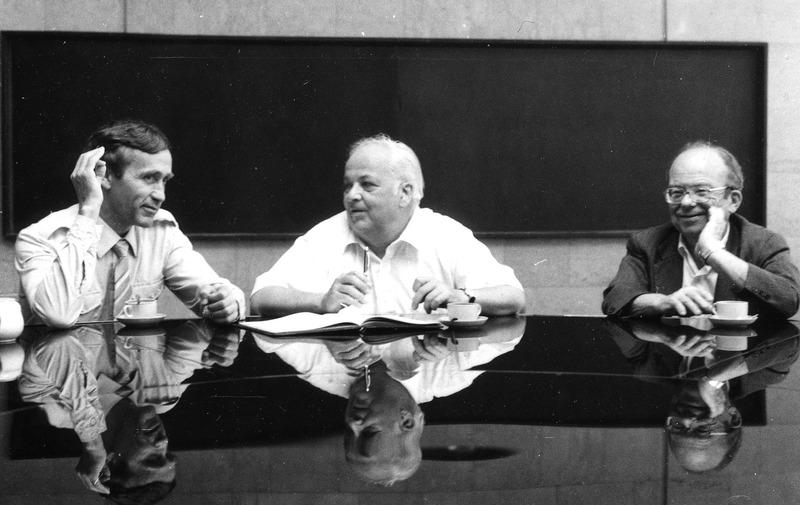 Sasha Skrinsky, Burton Richter and W. K. H. Panofsky seated at table in front of  blackboard, August 1986